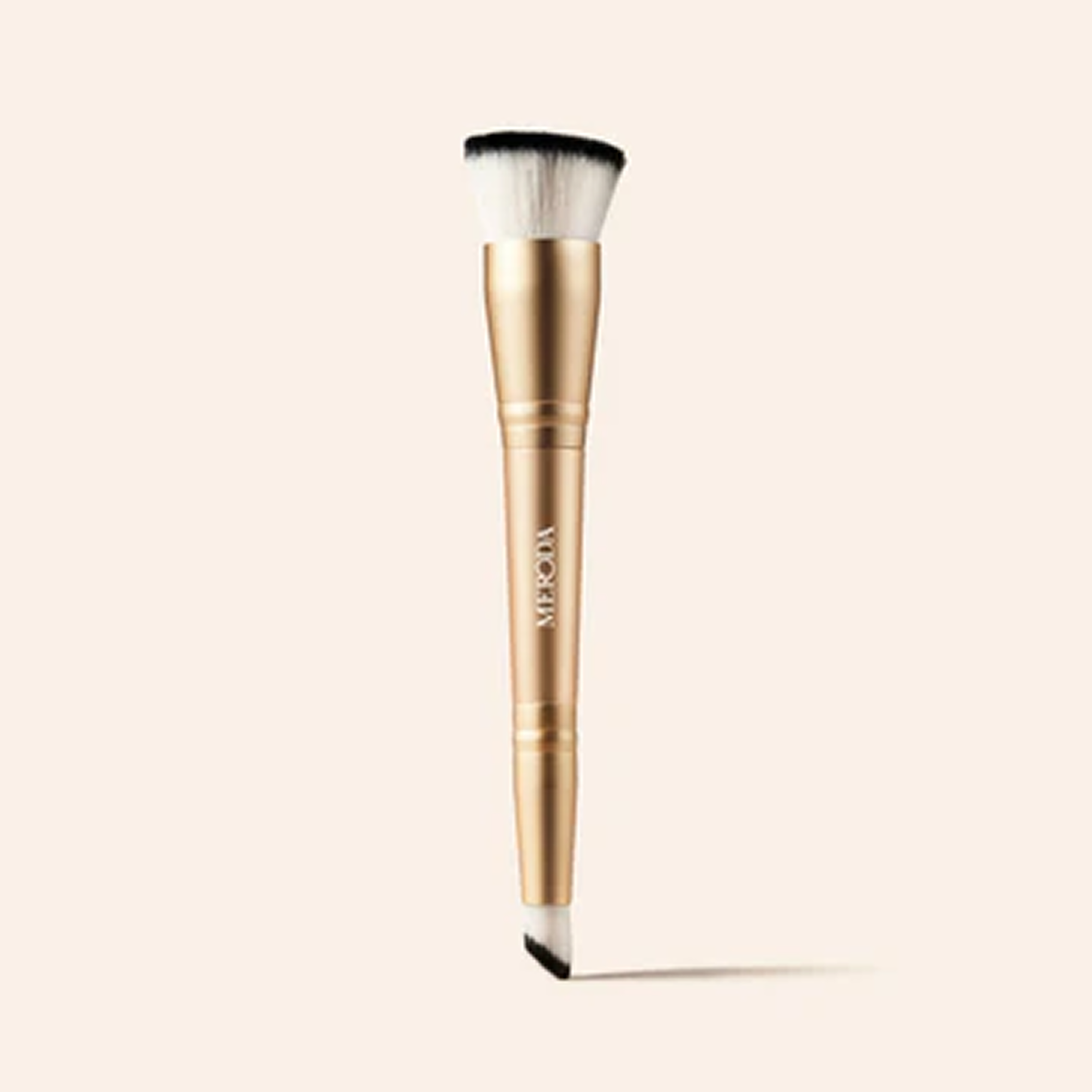 Dual-ended makeup brush with gold handle on a light background.