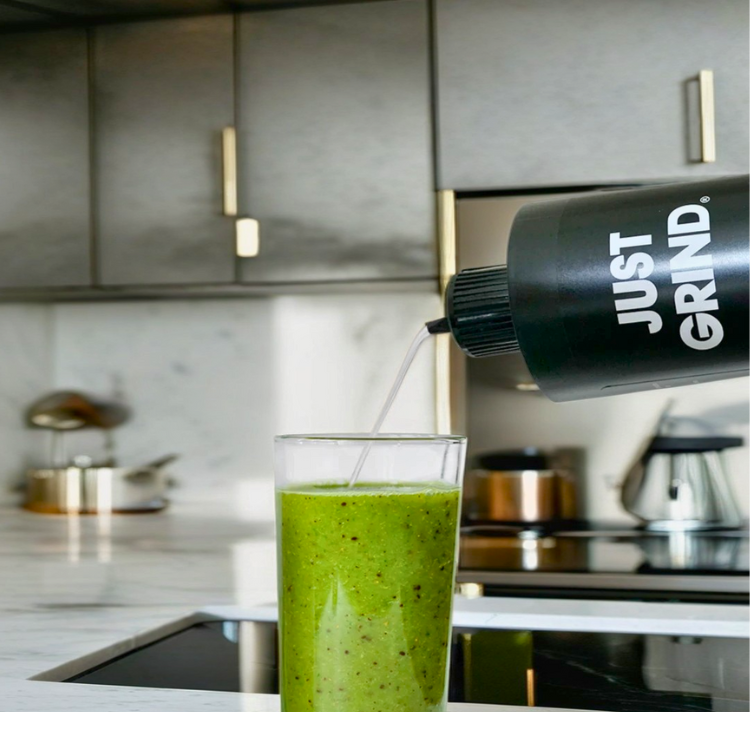 Green smoothie being poured into a glass in a modern kitchen.