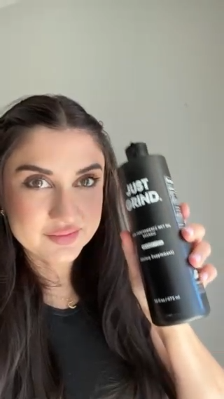 Person holding a black bottle labeled 'Just Grind' against a plain background.