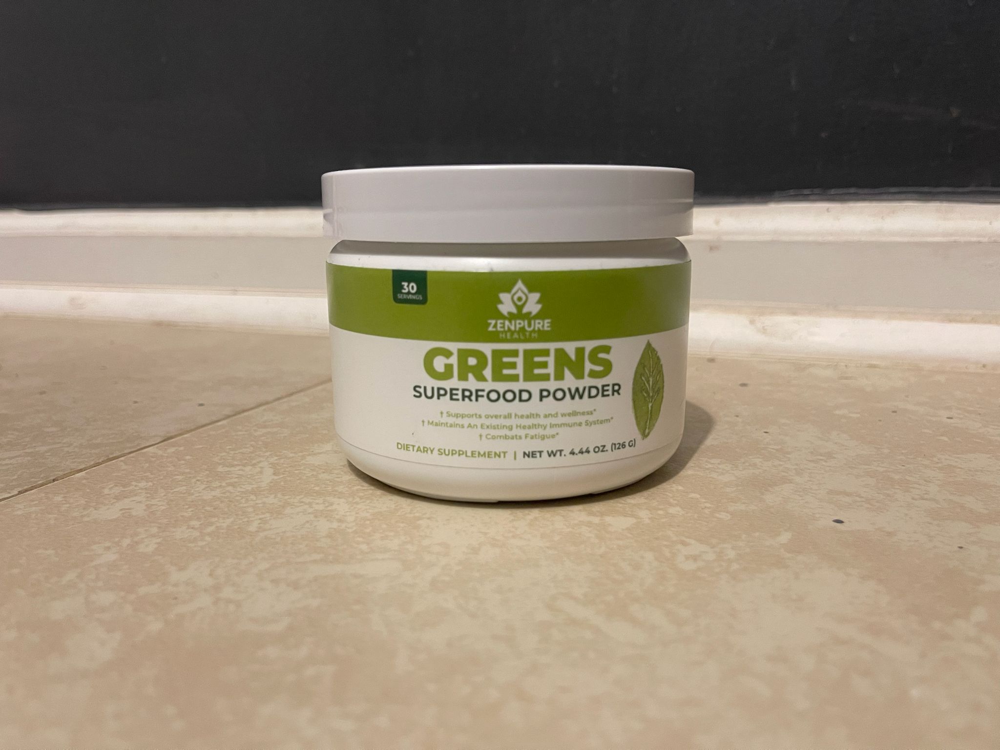 Container of greens superfood powder on a tiled surface.
