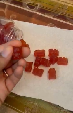 Red gummy bears scattered on a white surface, with a hand holding one.