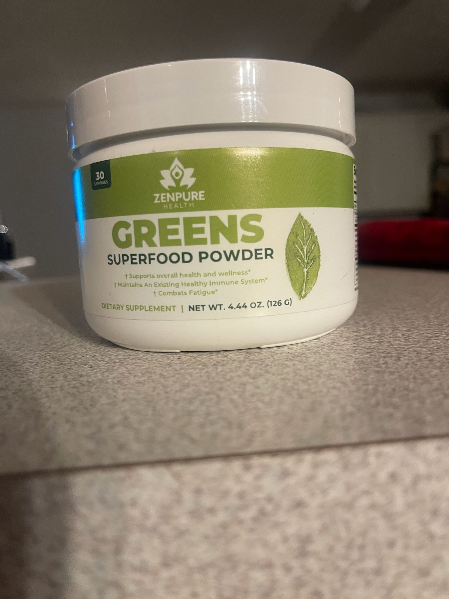 Container of Zenpure Health Greens Superfood Powder on a countertop.