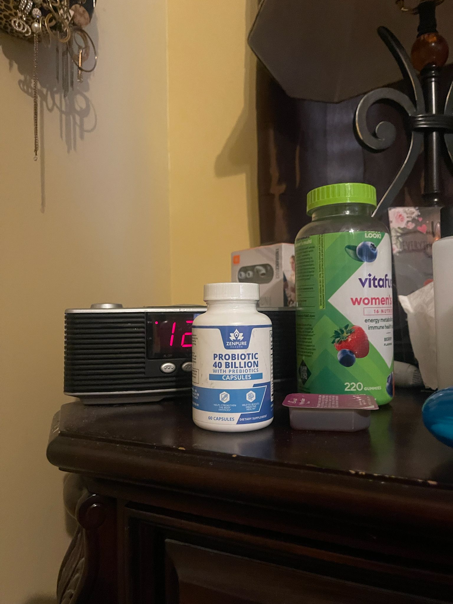 Nightstand with probiotic bottle, vitamin gummies, clock, and lamp.