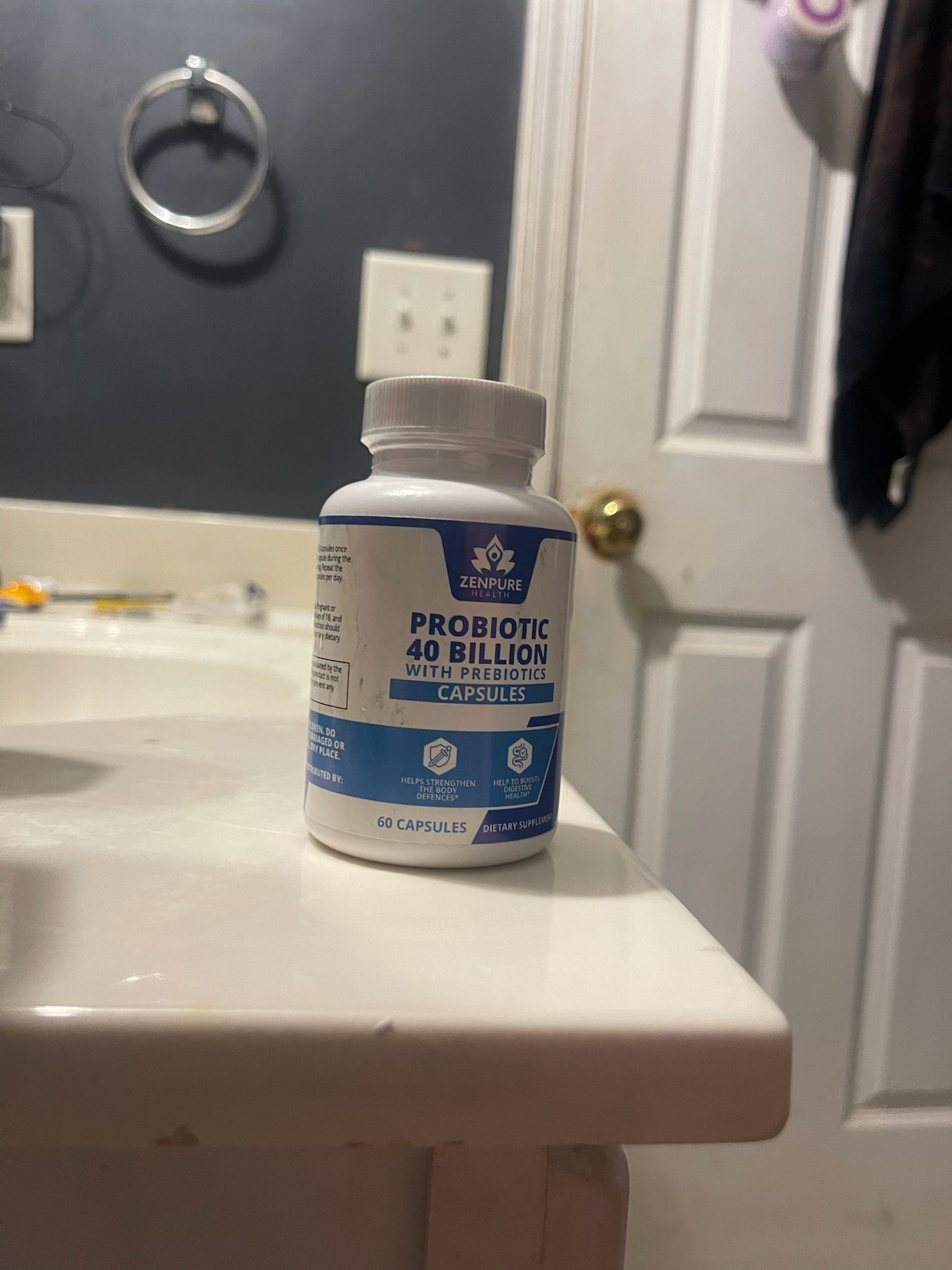 Probiotic supplement bottle on bathroom counter near a closed door and light switches.