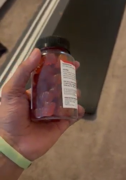 A hand holding a jar filled with gummy vitamins.
