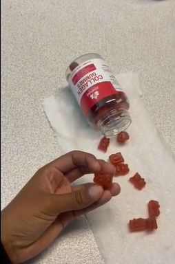 Hand holding red gummy near a tipped bottle on a paper towel.