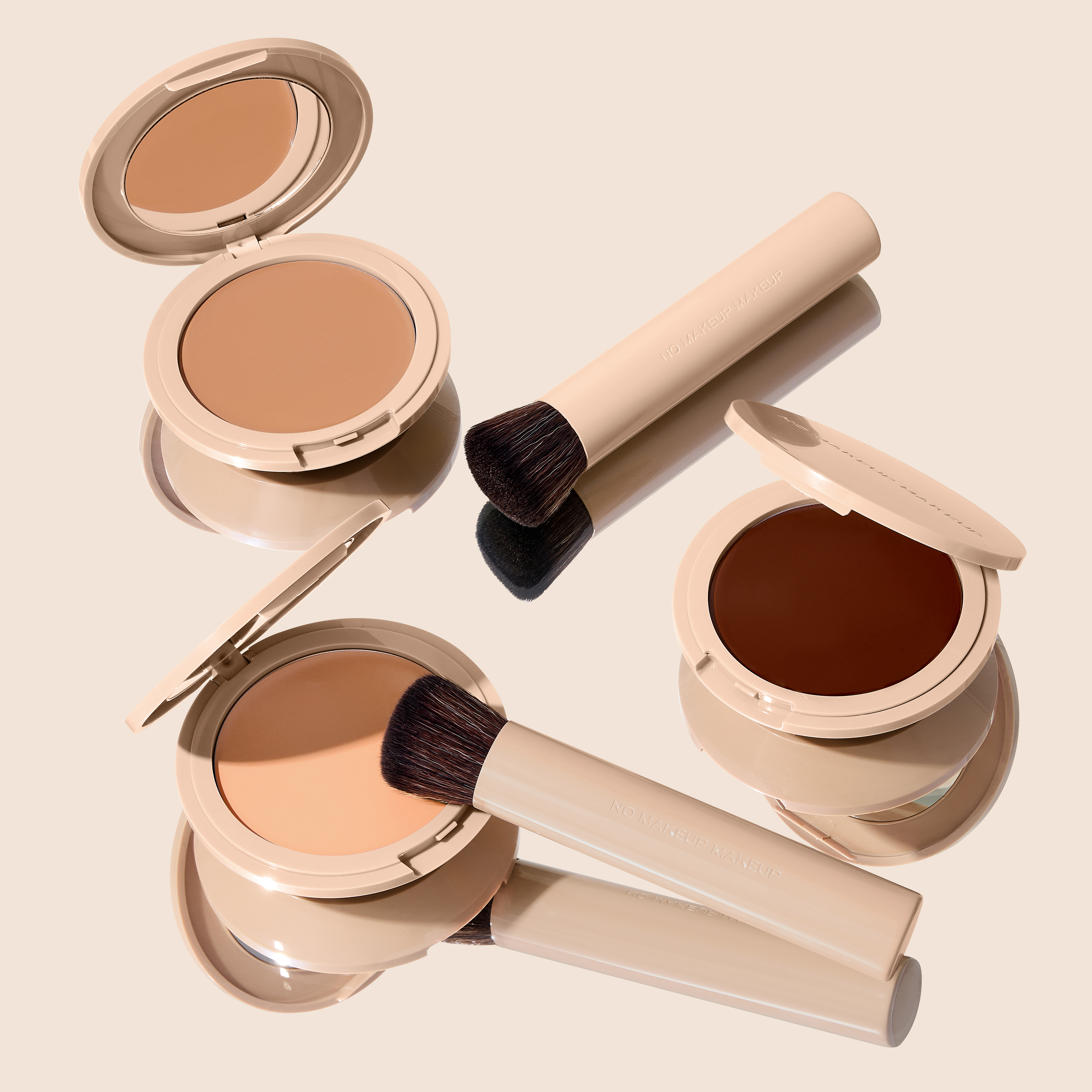 An arrangement of beige makeup compacts and brushes in various shades on a reflective surface.