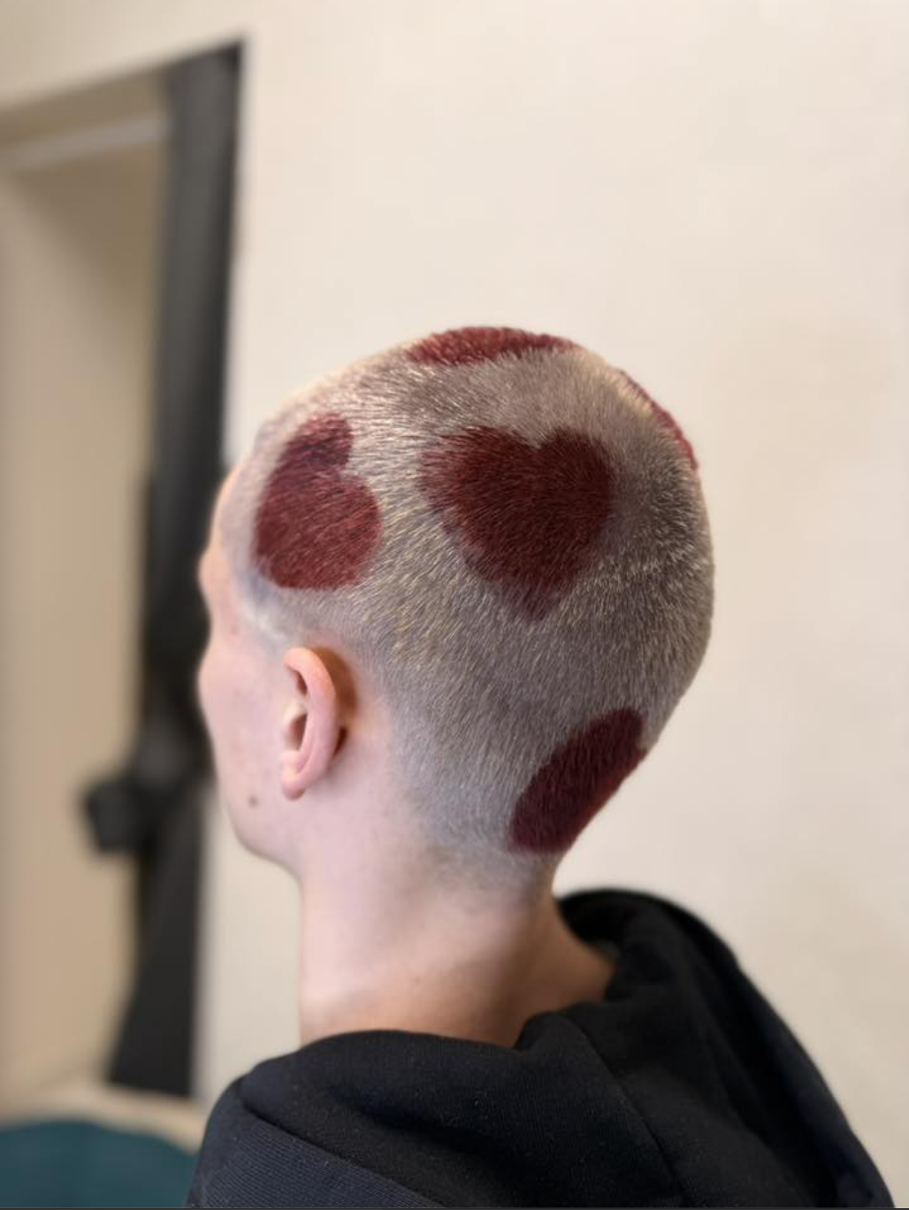 The back of a person's head with short hair dyed with a pattern of red hearts.