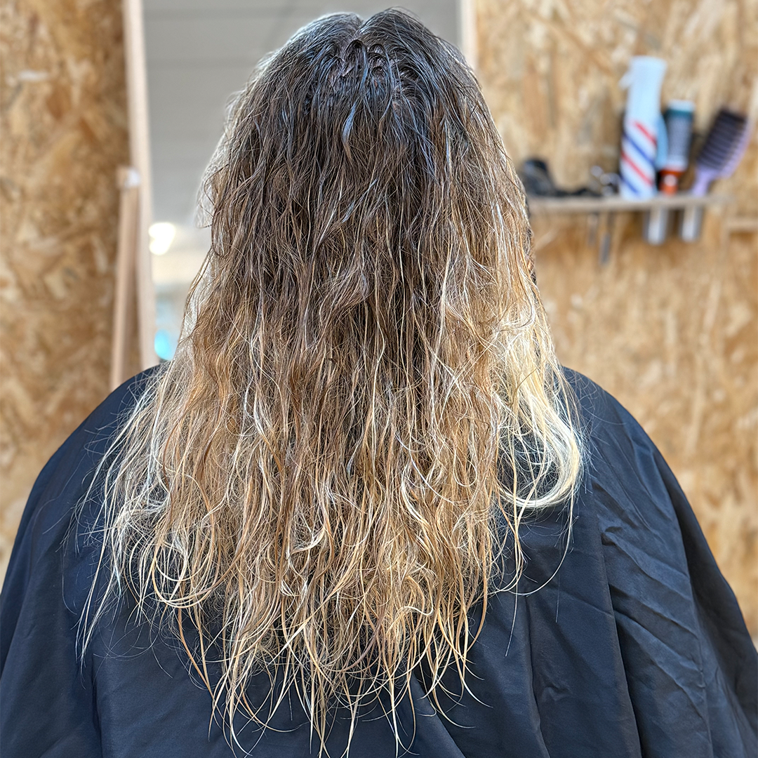Person with long, wavy hair viewed from the back in a salon setting.