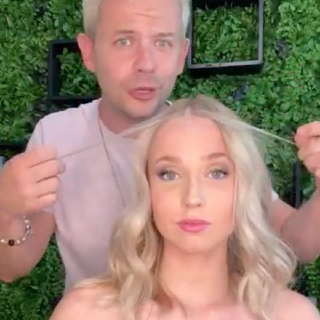 Person styling another person's hair in front of a leafy background.