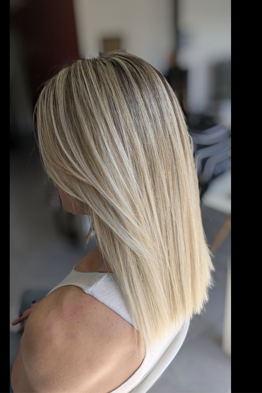A rear-side view of a woman with straight, shoulder-length blonde hair with highlights.