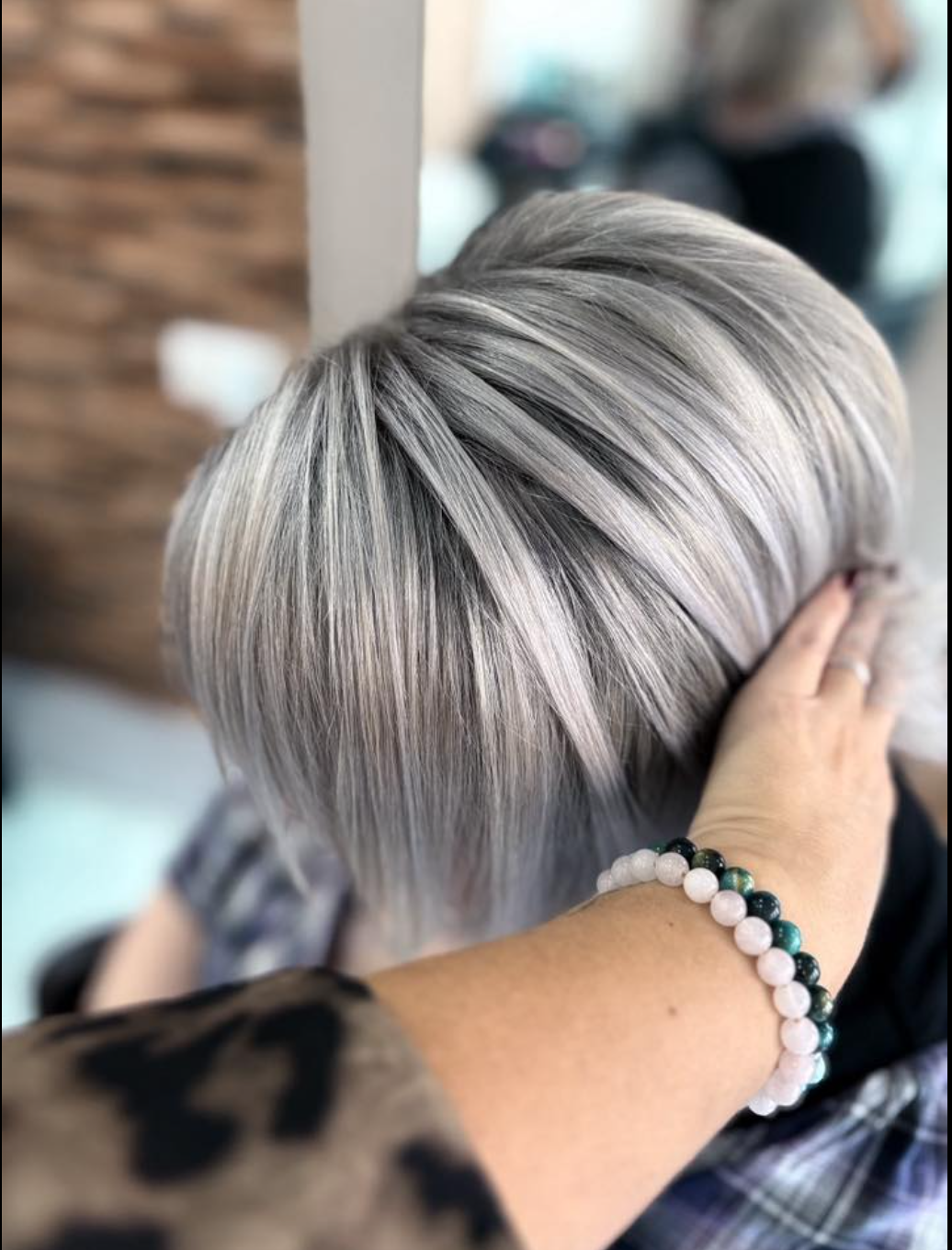 A close-up of a person's short, sleek, silver-grey hair being styled by a hand with a bracelet.