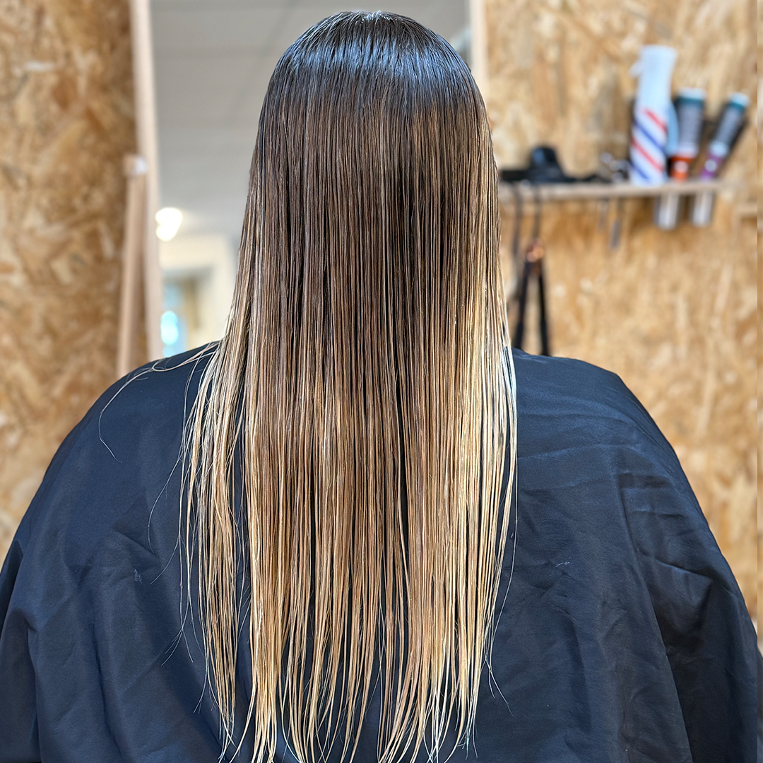 Person with long, wet hair in a hair salon, seen from behind.