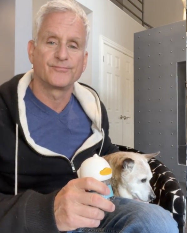 Man holding a toy, sitting with a dog on a chair.