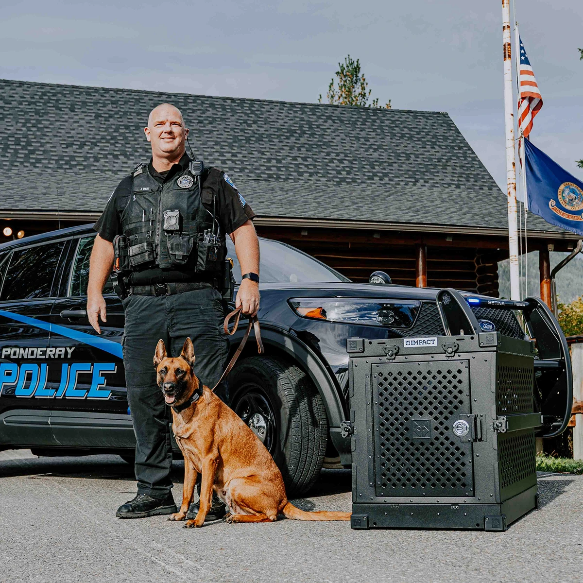 A Ponderay police officer and his K-9 dog stand beside a police car and a large crate.