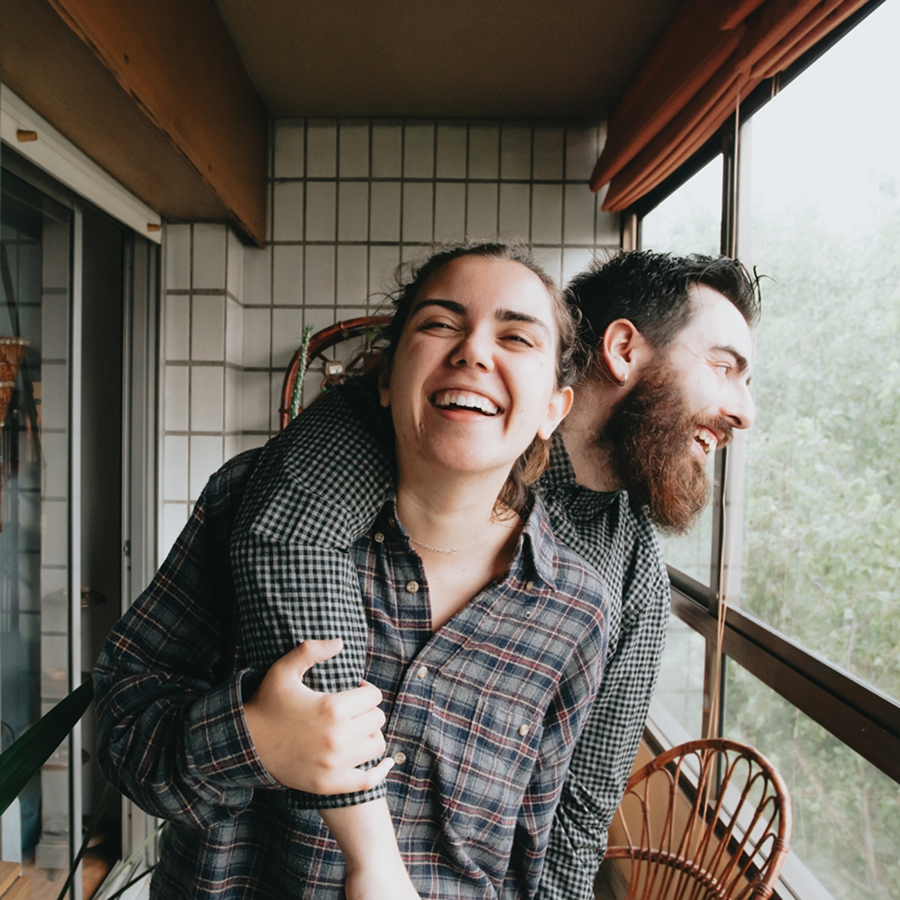 A man with his arm around a woman, both laughing together on a balcony.