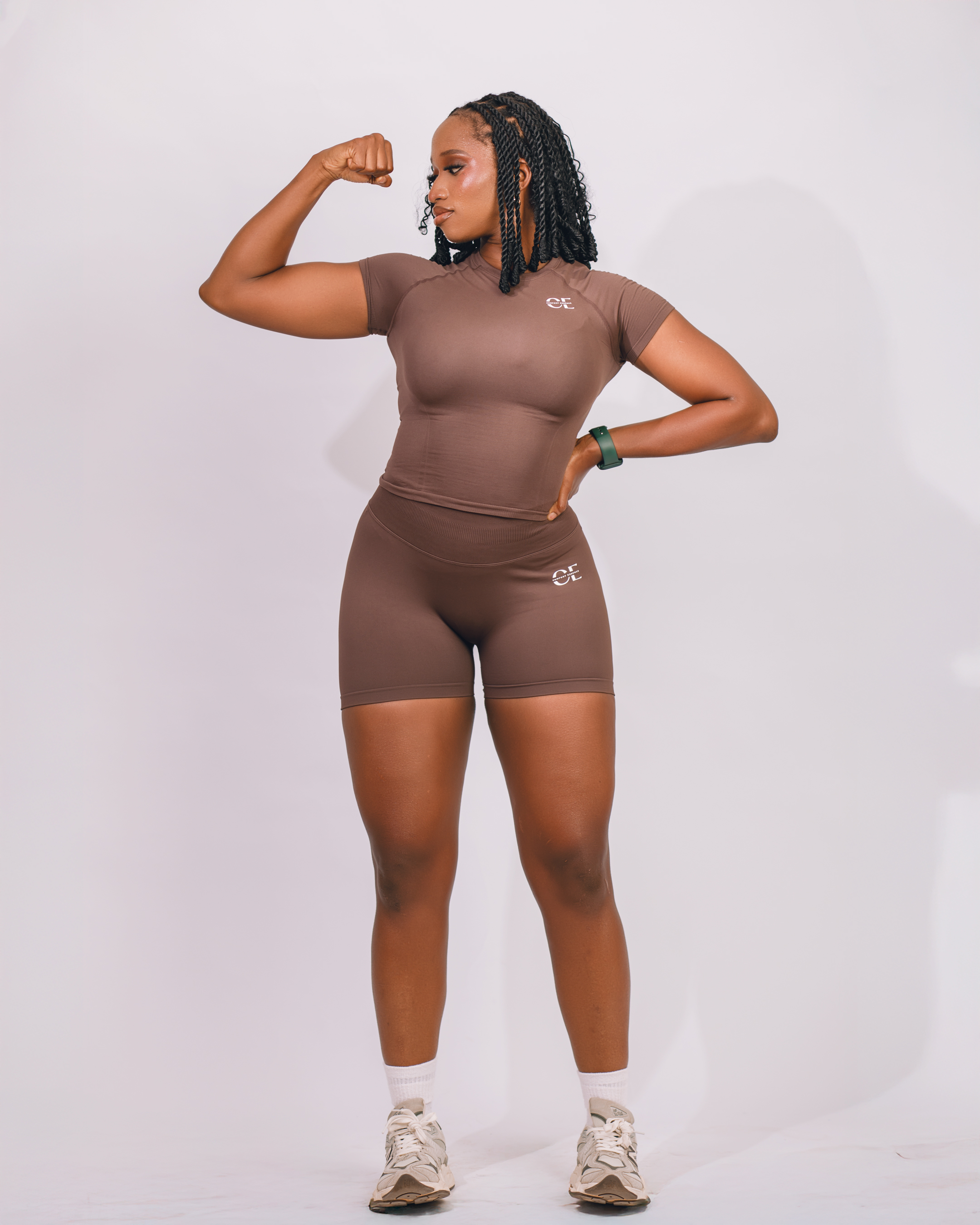 Person in athletic wear flexing arm muscles against a plain background.