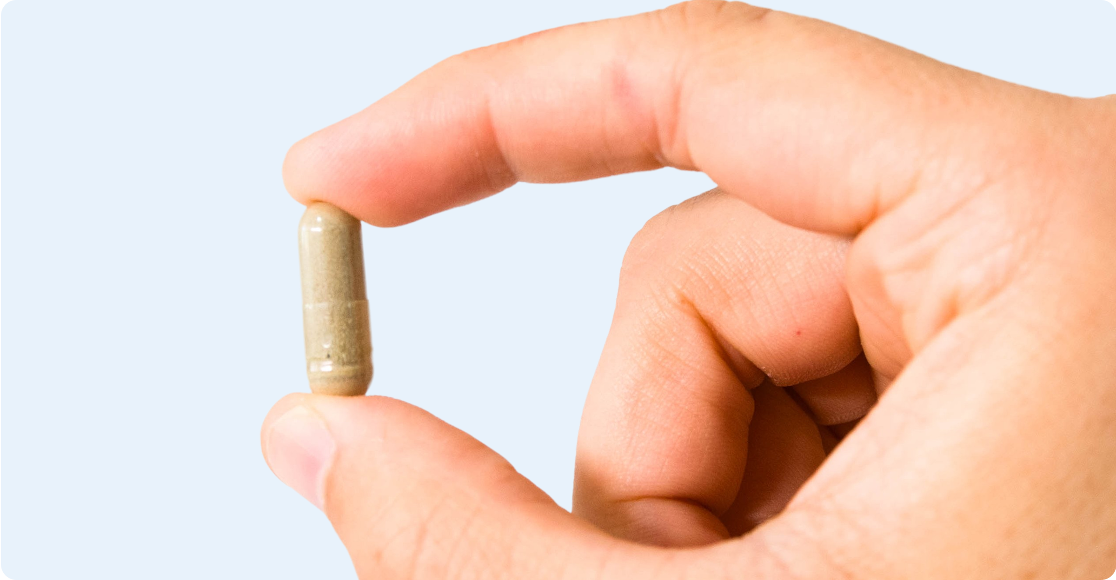 A hand holding a gray capsule pill between fingers.