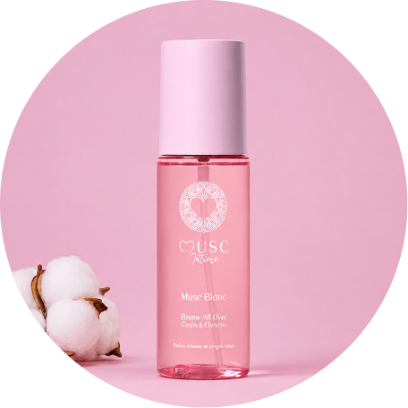 A bottle of Musc Intime body and hair mist next to cotton bolls on a pink background.