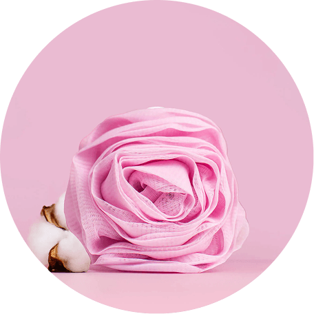 A pink rose-shaped bath loofah and two cotton bolls on a pink background.
