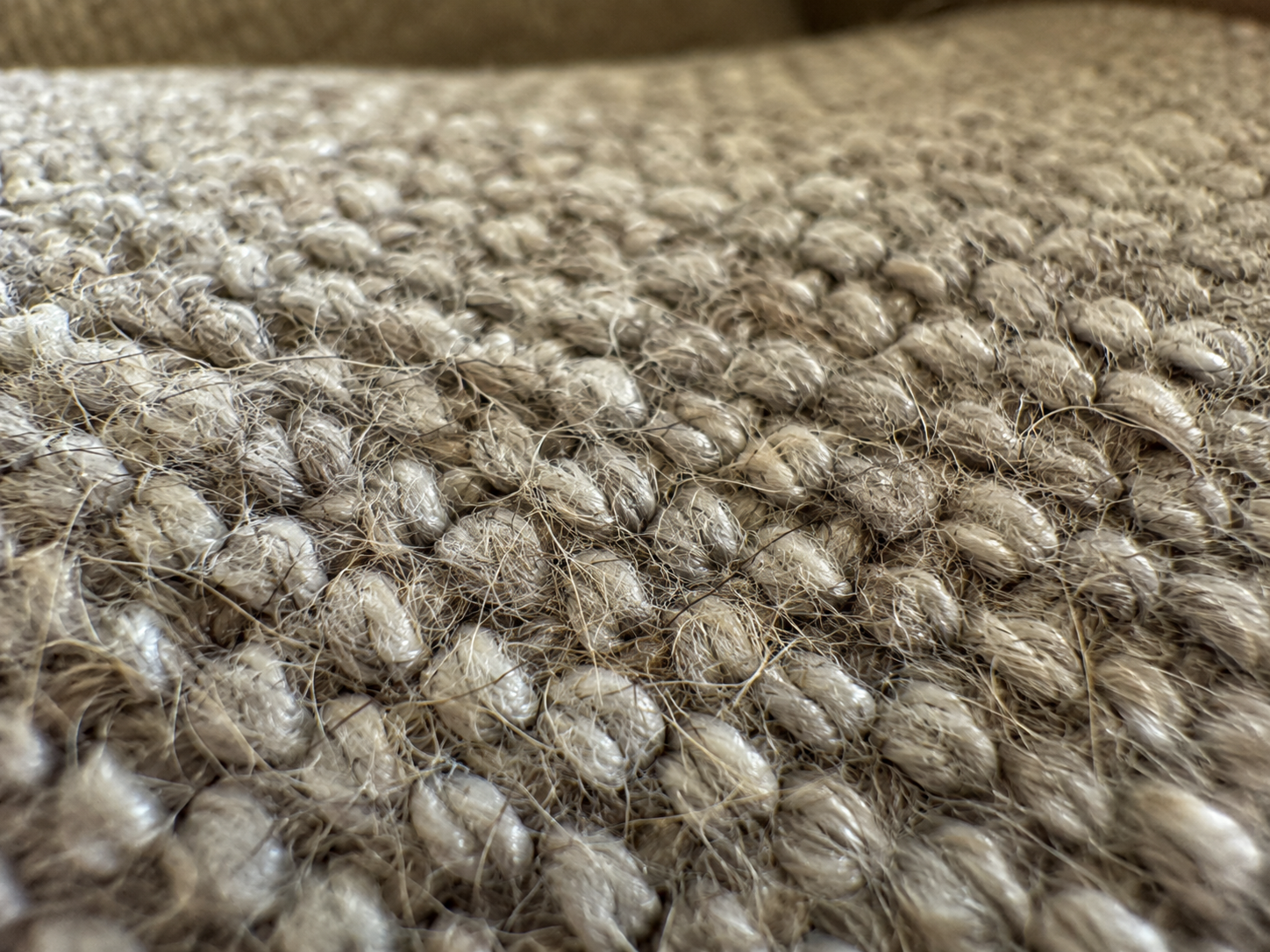 A macro, close-up shot of the textured weave of a beige or tan colored rug.