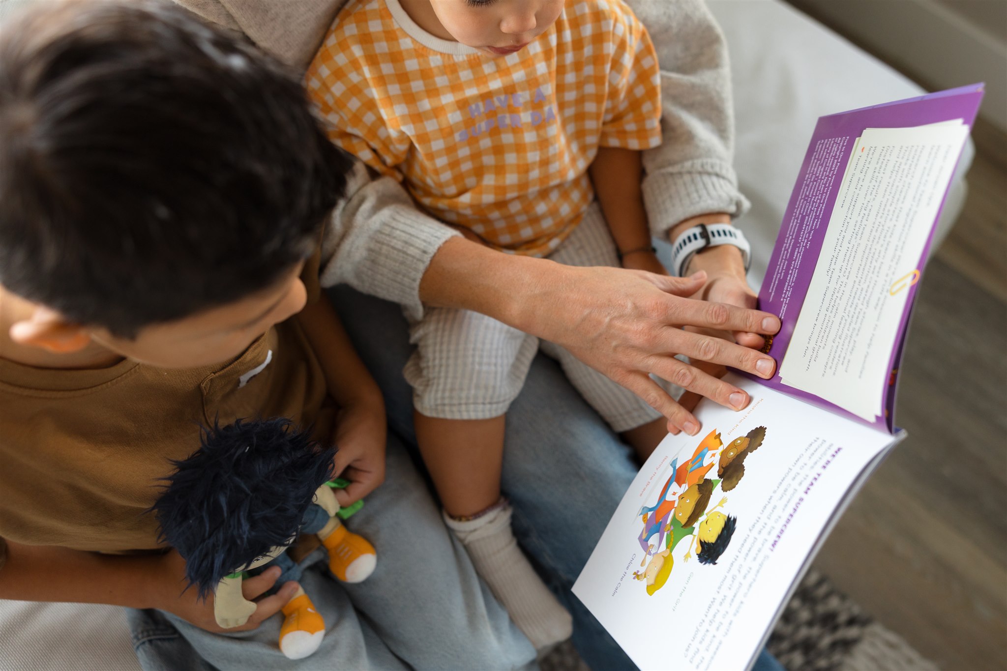 An overhead view of an adult and two children sitting together reading an illustrated book.