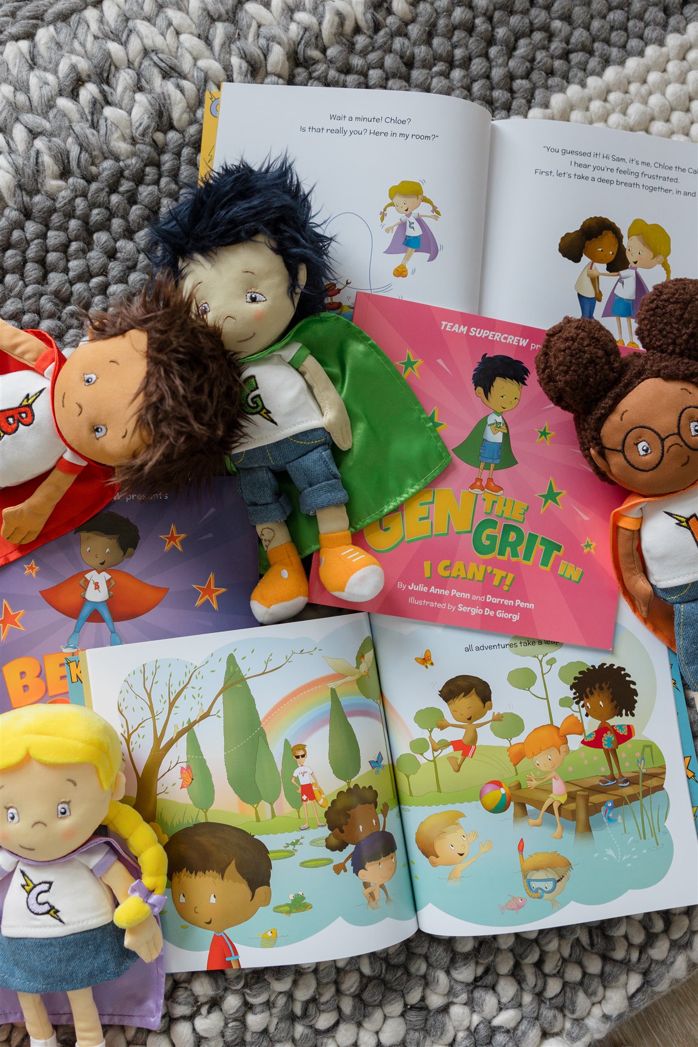 A collection of children's superhero books and matching plush dolls on a gray woven rug.