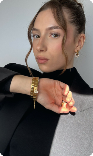 A woman with her hair up poses in a blazer, showing her gold bracelet and earring.