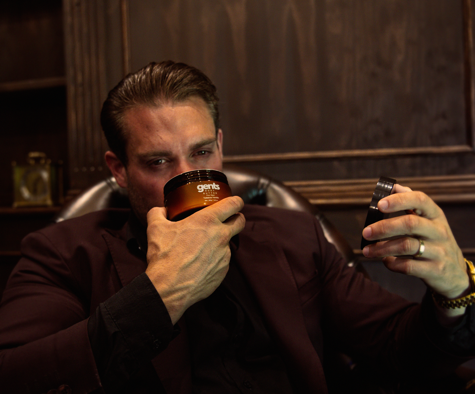 Man holding and smelling a jar labeled 'gents' in a dimly lit room.