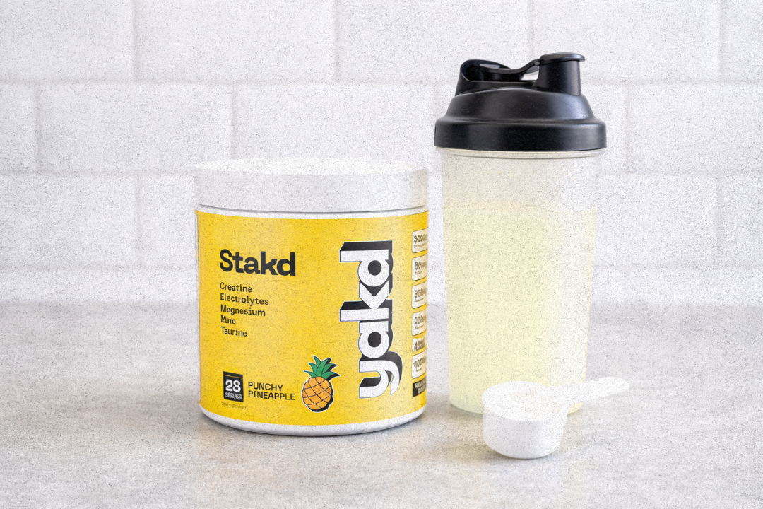 A tub of Stakd Jakd Punchy Pineapple supplement with a shaker bottle and a scoop of powder.