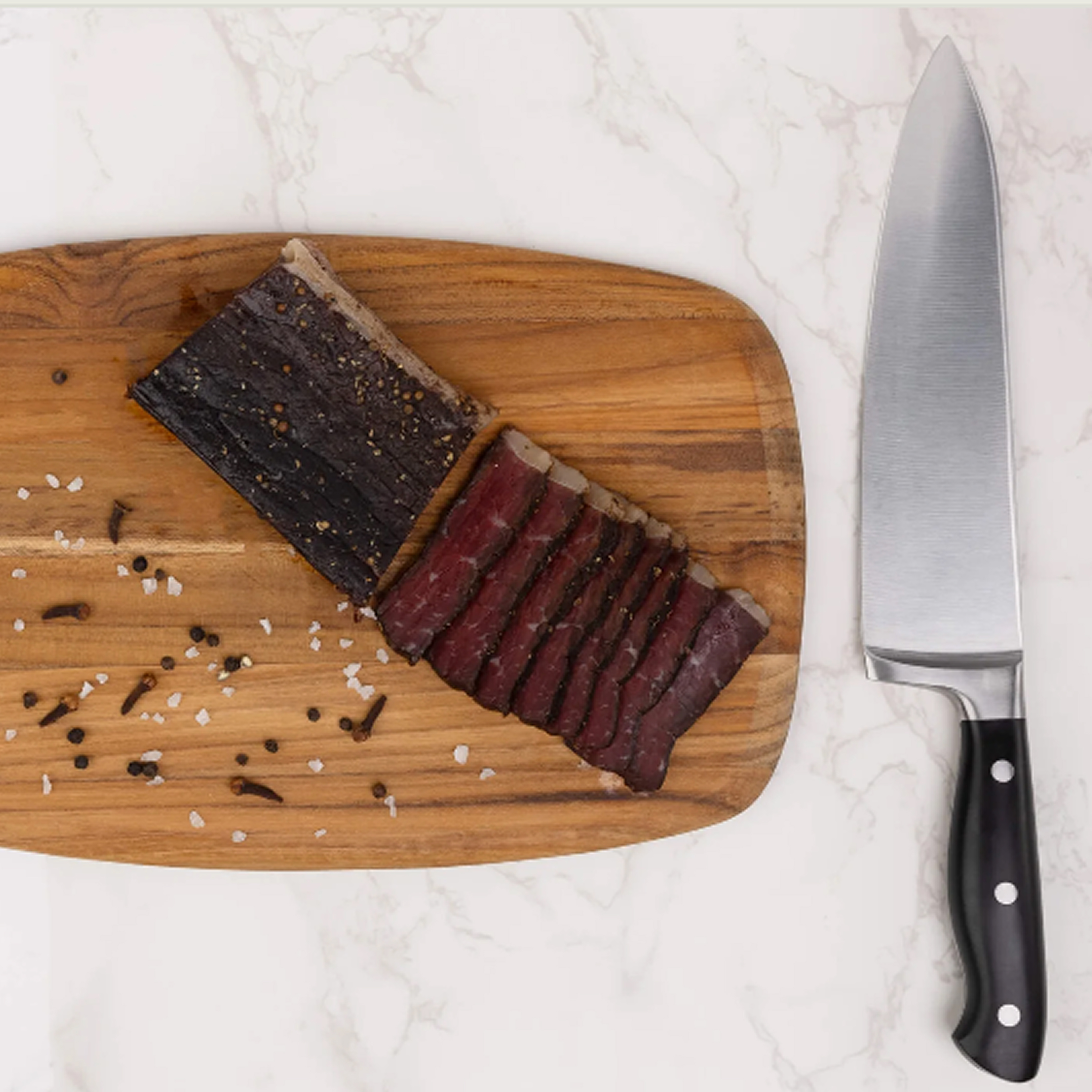 Sliced cured meat on a wooden board with a chef's knife.