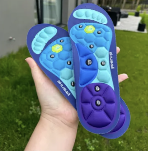 Hand holding two blue and purple insoles with massage nodes.