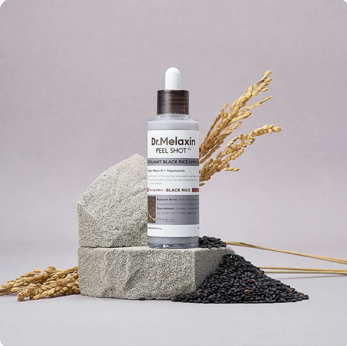 Skincare product bottle with black rice and wheat on textured stone.