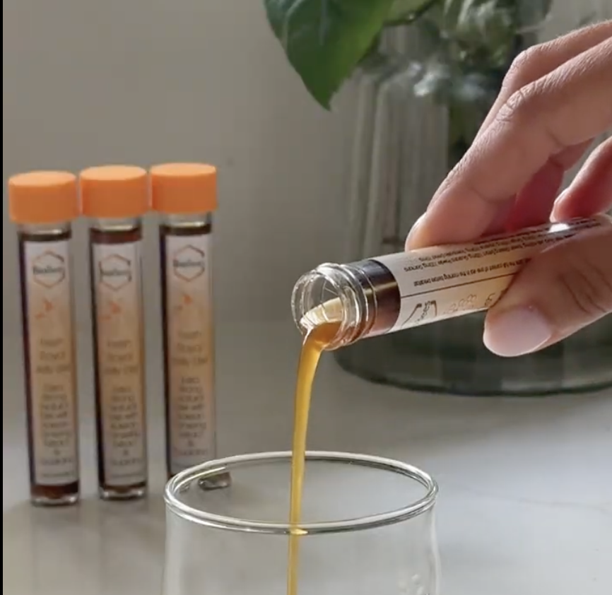 Hand pouring liquid from a vial into a glass, with vials in the background.