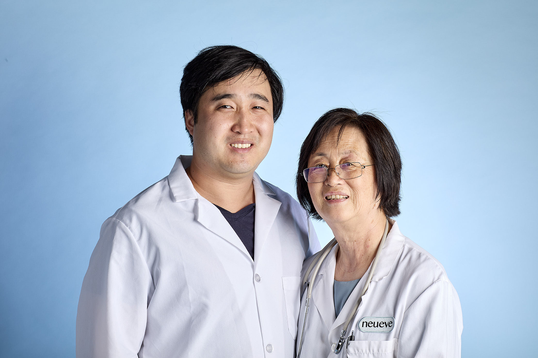 Two people in lab coats smiling against a blue background.