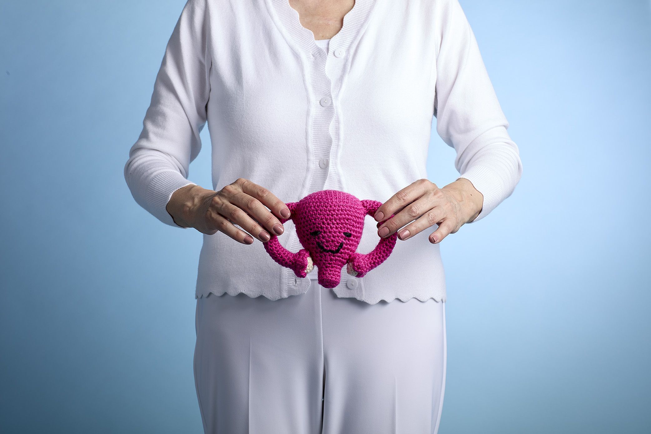Person holding a crocheted pink uterus toy against a blue background.