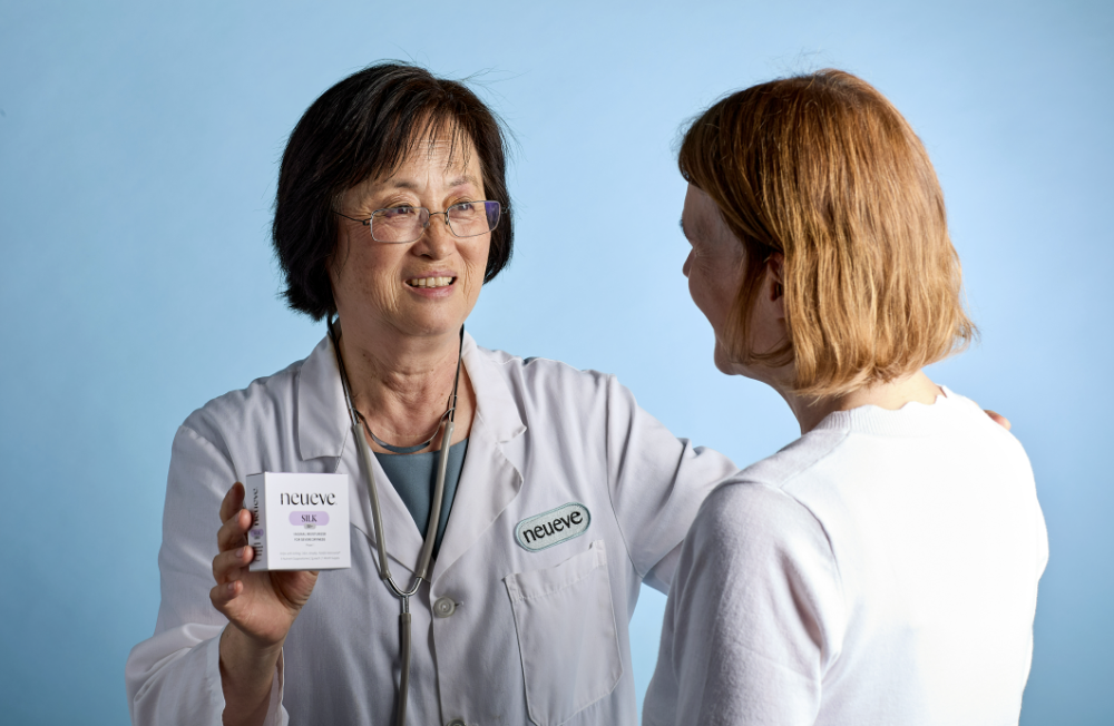 Person in lab coat shows product box to another person.