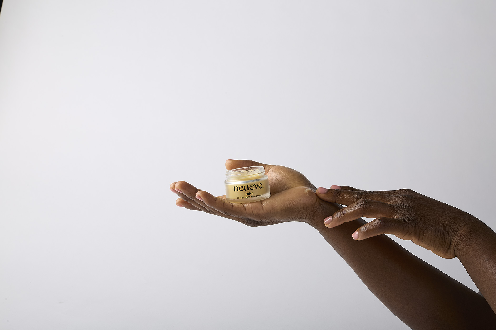 Hands holding a small jar of salve against a plain background.