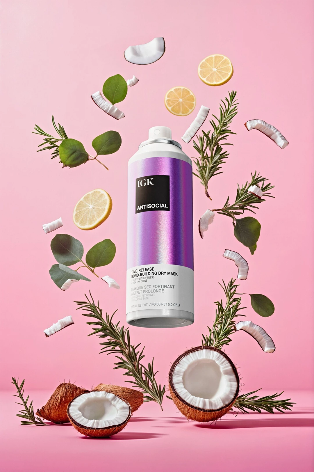 A can of IGK dry mask floats with coconuts, lemons, and herbs against a pink background.