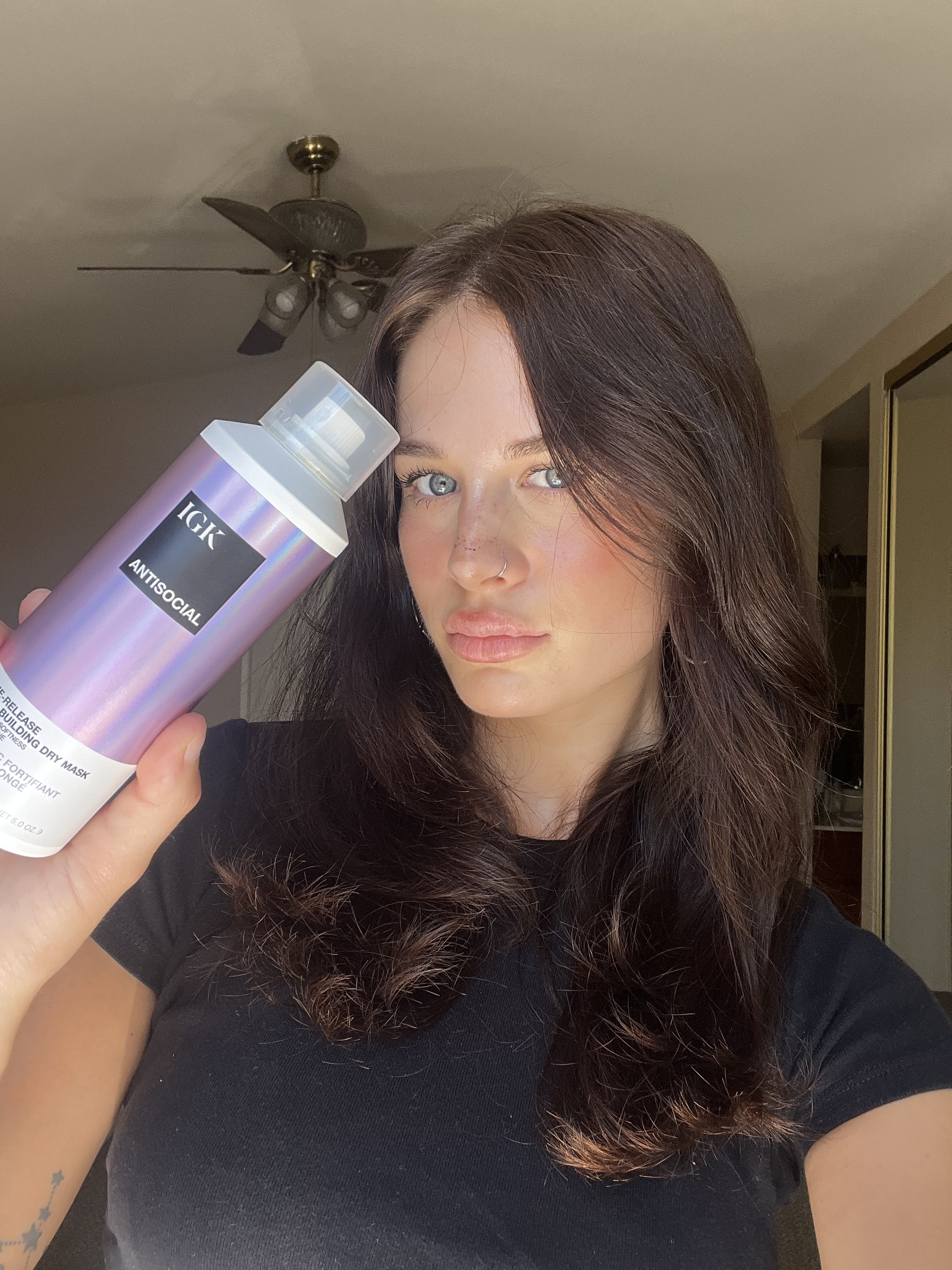 A woman with long dark hair holds up a can of IGK hair product called Antisocial.