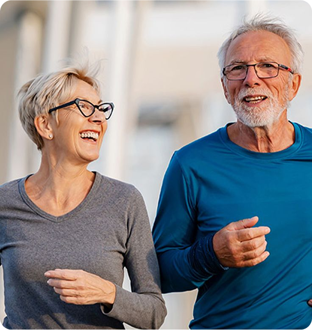 Two older adults jogging and smiling outdoors.