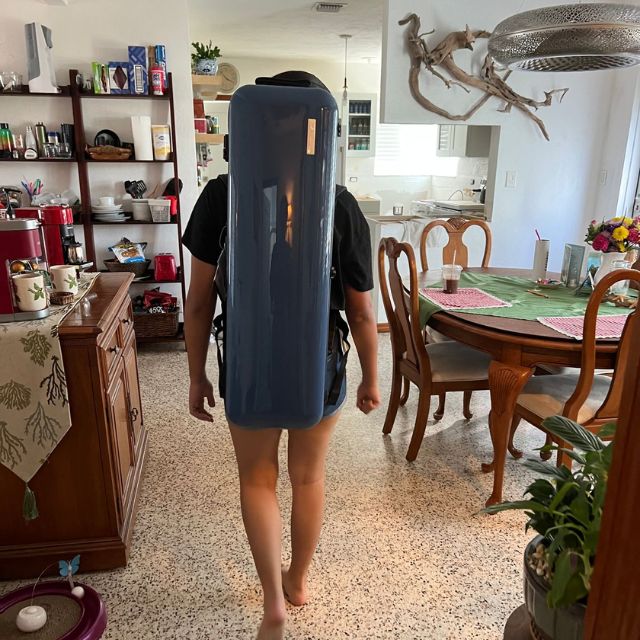 Person carrying a large blue suitcase on their back in a dining room.