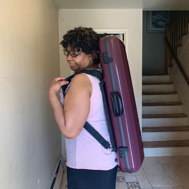 Person wearing a large maroon case on their back, standing in a hallway.