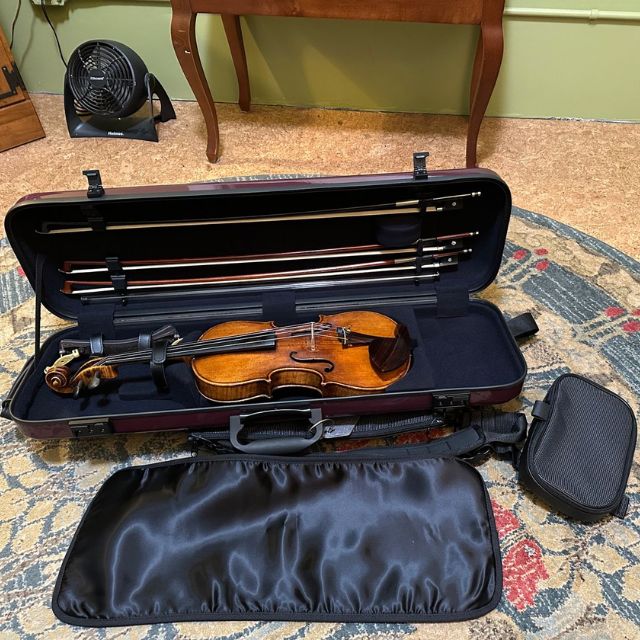 Open violin case with violin and bows on a patterned rug.