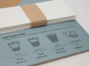 A stack of laundry detergent sheets sits on top of an instruction card with illustrated load sizes.