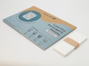 A cardboard package of laundry detergent sheets next to a stack of the white sheets.