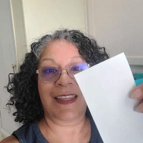 A smiling woman with curly graying hair and glasses holds up a blank white card.