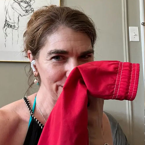 A woman holds a piece of red fabric up to her face, partially covering her mouth and nose.