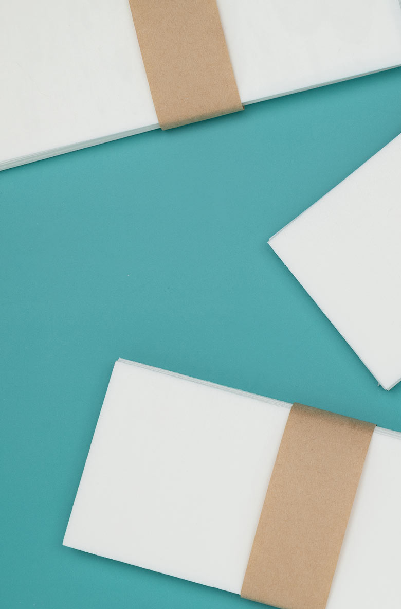 An overhead view of stacks of white paper with brown paper bands on a teal background.