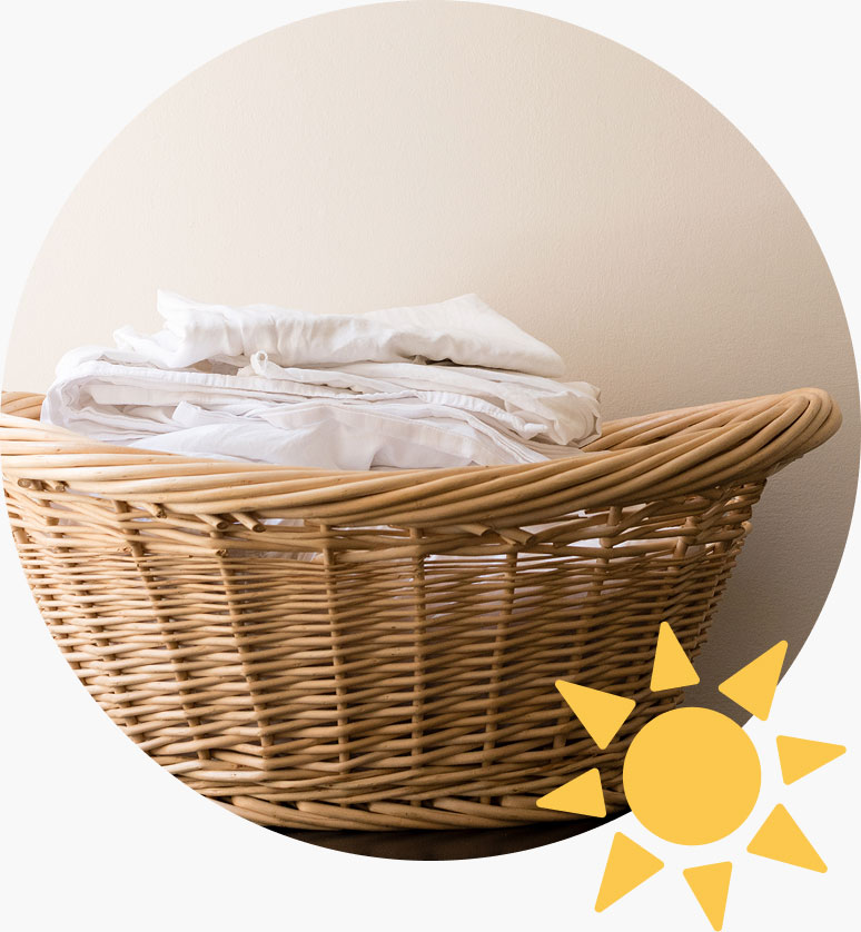 A wicker laundry basket full of folded white linens, with a graphic of a yellow sun.